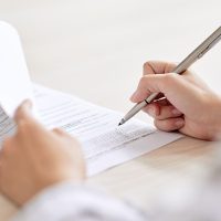 Crop shot of person with pen signing contract at desk in daylight